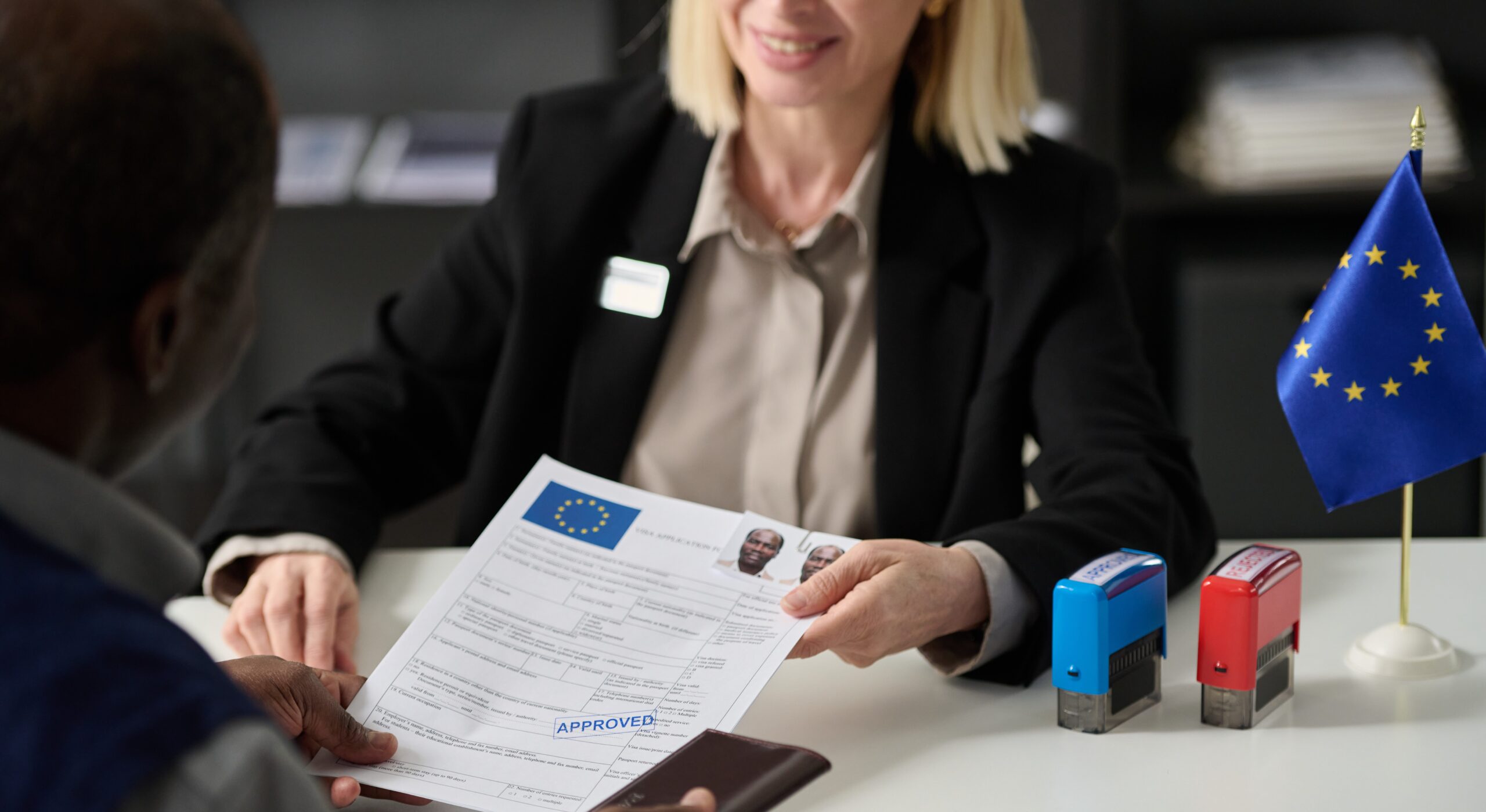 close-up-of-smiling-woman-handing-approved-visa-2025-03-18-22-23-47-utc Close up of smiling woman handing approved visa application form to black man in immigration office